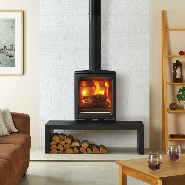 wood burning stove on a table with logs stacked underneath in a stylishly clean white room